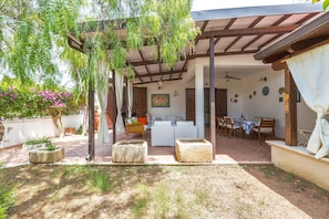 An outdoor patio area with a covered seating area, a dining table, and potted plants.