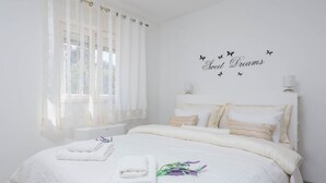 A bedroom with a bed, white curtains, a wall decoration with butterflies, and a bedside lamp. - Apartment Lana (Supetar)