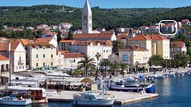 A coastal town with a prominent church tower, a marina with boats, and buildings with red-tiled roofs. - Apartment Lana (Supetar)