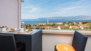 A balcony with a table set for breakfast, overlooking a coastal town with buildings and a clear sky. - Apartment Lana (Supetar)
