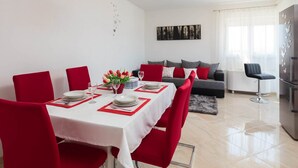A dining area with a white table set for four, red chairs, a vase of tulips, and a modern pendant light. - Apartment Lana (Supetar)