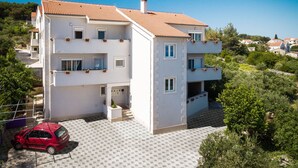A multi-story residential building with a tiled roof, balconies with potted plants, and a paved driveway. - Apartment Lana (Supetar)
