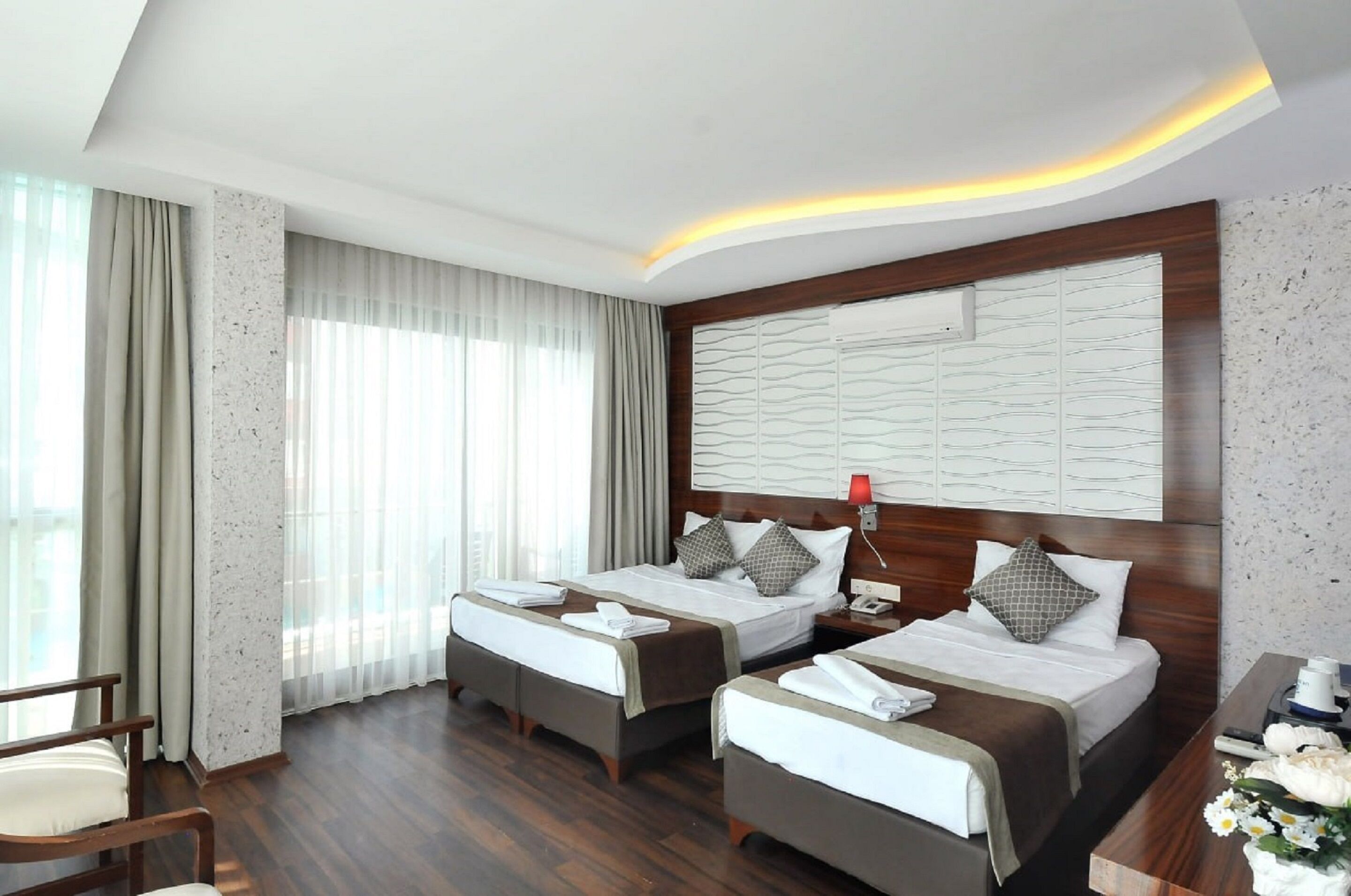 Una habitación de hotel con dos camas, un escritorio, una silla y un ventanal con cortinas.