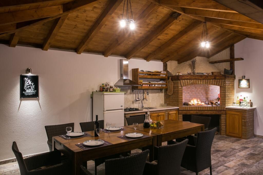 A rustic dining area with a wooden table set for four, a brick fireplace, and a kitchen with a chimney.