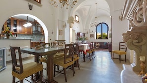 Un vaste espace de salle à manger avec une longue table et des chaises, une cuisine dotée de meubles en bois et un lustre.