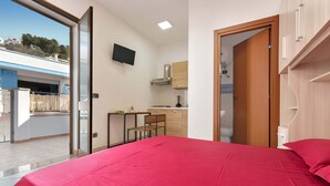 A bedroom with a large bed, a desk, and a kitchenette in the background. - 2214 Villetta Enea - Mono 1 by Barbarhouse (Castro)