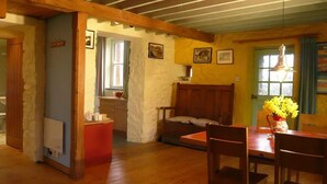 Una habitación acogedora con techo de madera, una mesa de comedor con sillas, un sofá y una ventana con cortinas.