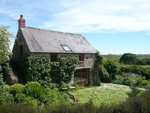 Une maison en pierre avec un toit en pente, de grandes fenêtres et une cheminée.