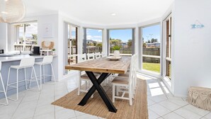 Une cuisine lumineuse avec une table à manger en bois, des chaises blanches et une vue sur le jardin à travers de grandes fenêtres.