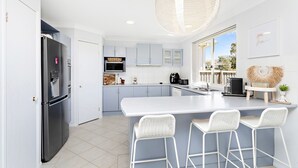 Une cuisine moderne dotée d’un grand îlot central, de tabourets de bar blancs et offrant une vue sur l’extérieur.