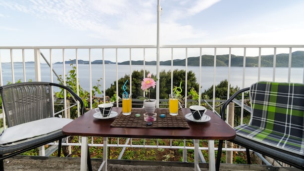 A balcony with a table set for two, overlooking a body of water and hills.
