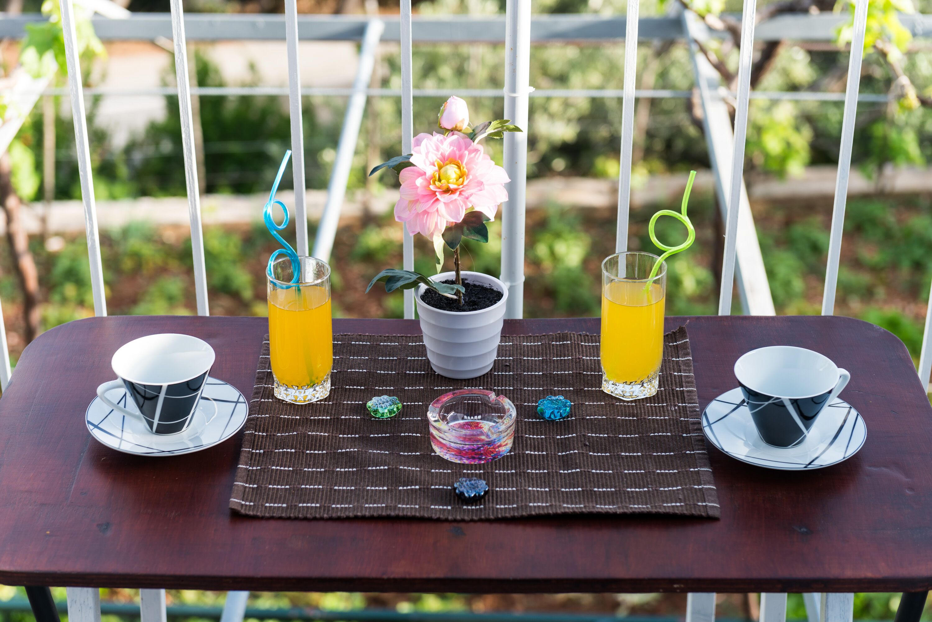 Una mesa de madera con dos tazas y dos vasos de zumo de naranja, una planta en maceta y un pequeño recipiente de vidrio.