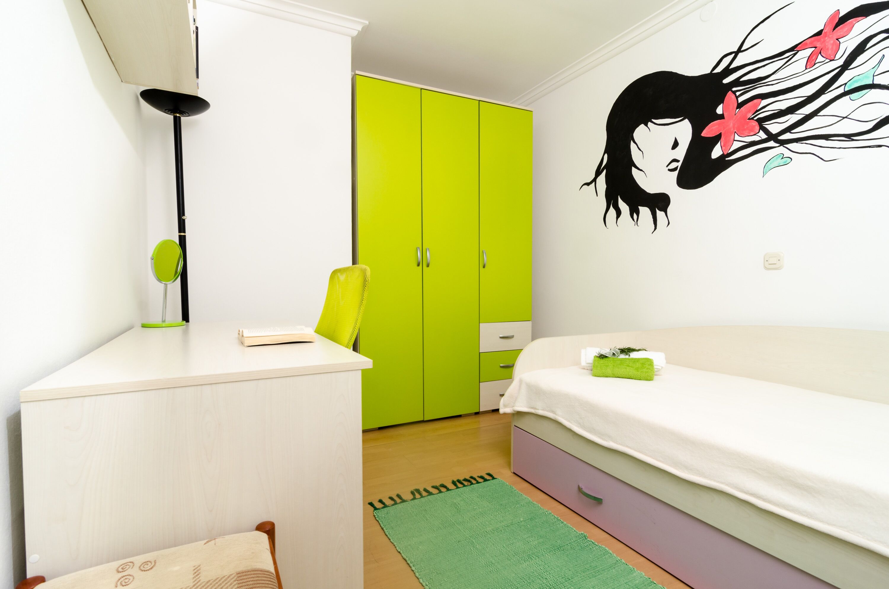 A bedroom with a bed, a desk, a chair, a wardrobe, and a wall decoration.