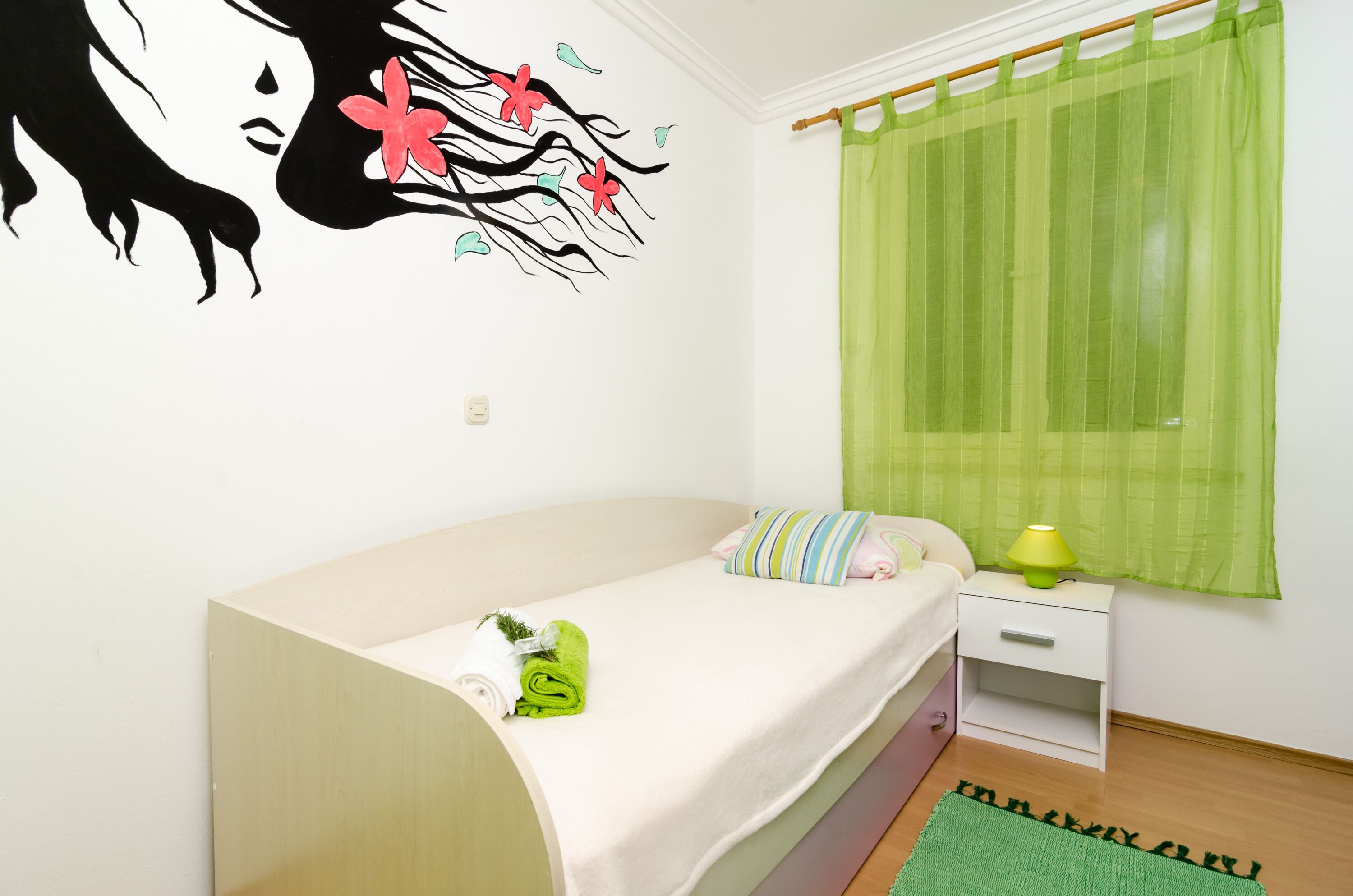 A single bed with a green towel, a striped pillow, and a nightstand with a lamp.