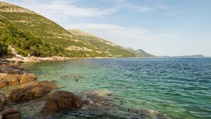 A coastal landscape with clear waters, rocky shore, and a mountainous backdrop.