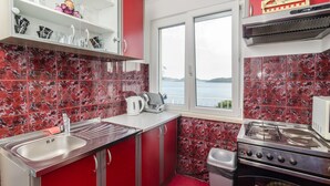 A kitchen with red cabinets, a stainless steel sink, a gas stove, and a window overlooking a body of water.