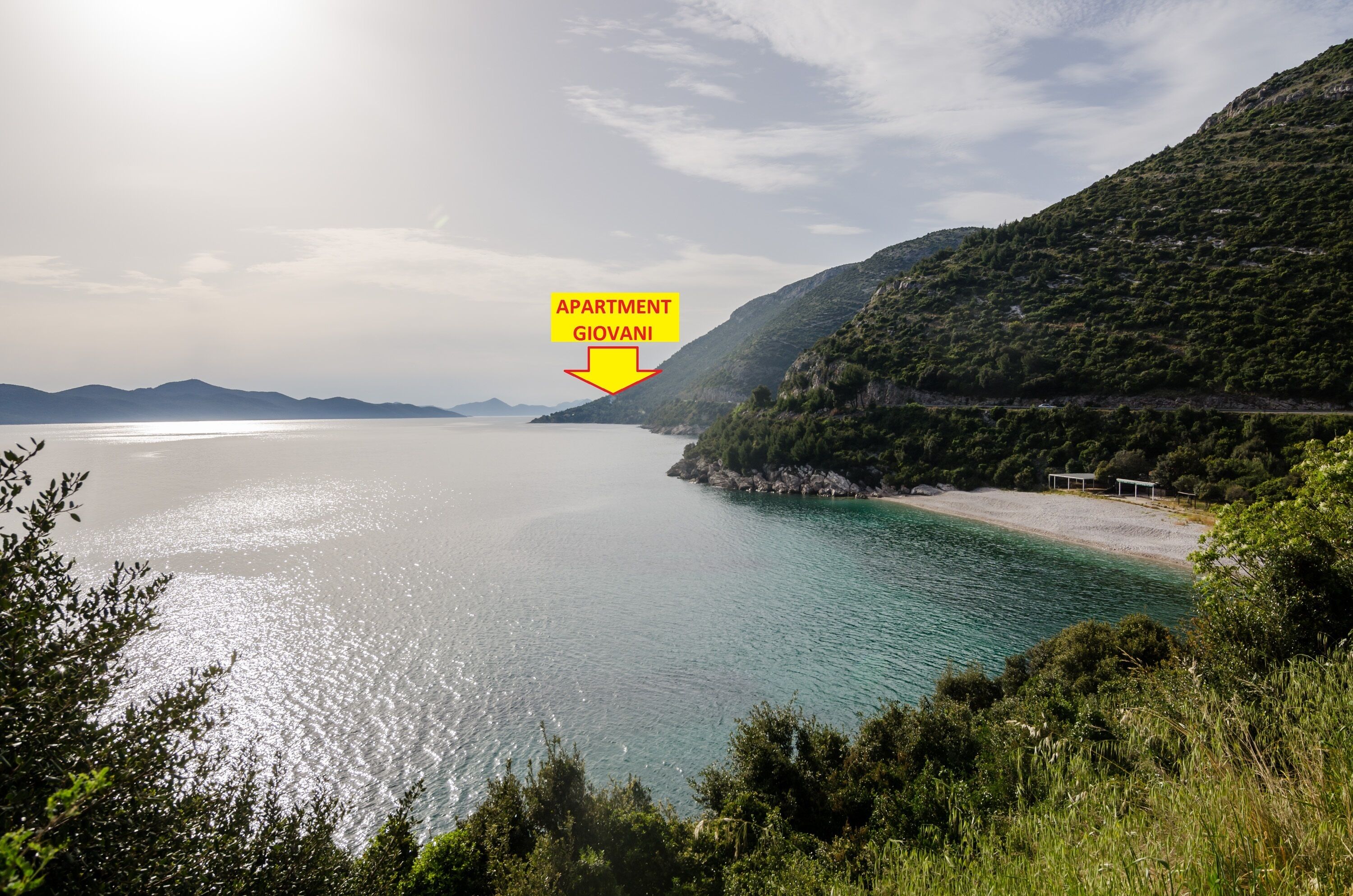 A coastal landscape with a clear view of the sea, a beach, and a mountainous backdrop.