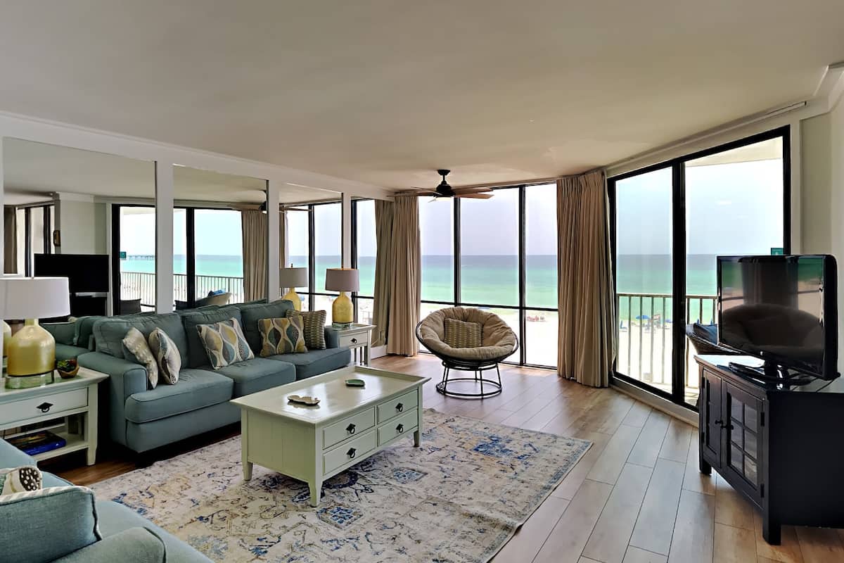 Ein geräumiges Wohnzimmer mit großem Fenster und Meerblick, ein bequemes Sofa, ein Couchtisch und ein Fernseher.