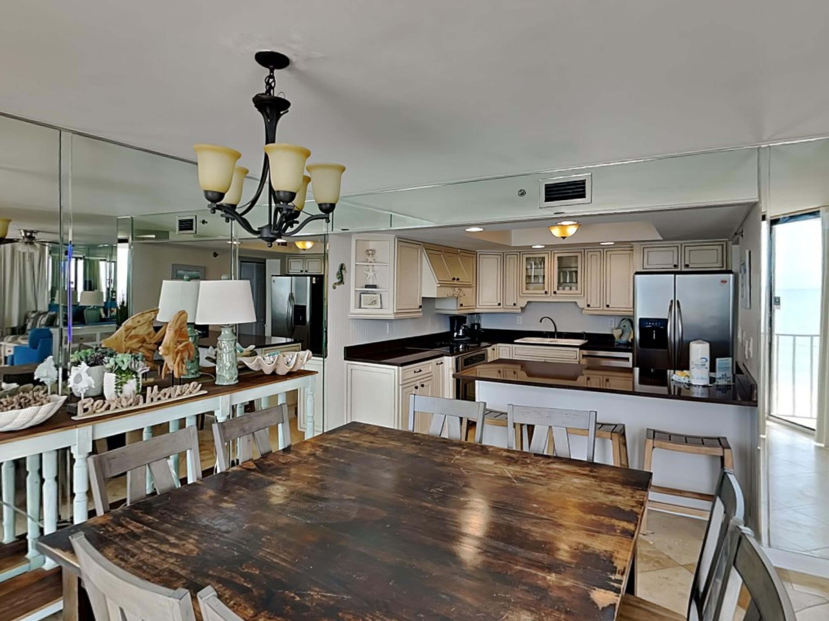 A modern kitchen with white cabinetry, a dark wooden dining table, and a chandelier.