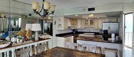 A modern kitchen with white cabinetry, a dark wooden dining table, and a chandelier.