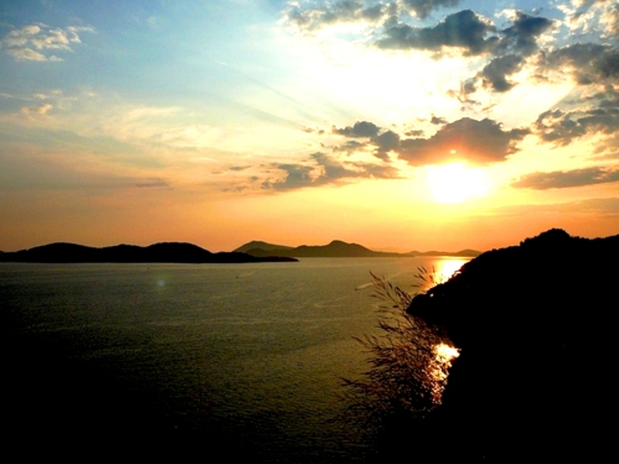 Un coucher de soleil sur une étendue d’eau calme, avec des reliefs terrestres visibles au loin.