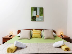 Ein ordentlich bezogenes Bett mit einem grünen Überwurf, mehreren Kissen und zwei Nachttischlampen.