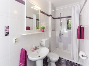 Ein Badezimmer mit einem weißen Waschbecken, einer Toilette und einer Dusche. Über dem Waschbecken befindet sich ein Spiegel und über der Dusche ein Fenster.