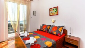 Un dormitorio con cama, mesita de noche, lámpara de pared y ventana con cortinas.