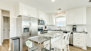 A modern kitchen with white cabinets, stainless steel appliances, a marble countertop, and a small bar area. - Seaside Sanctuary - Adorable Beach A-Frame, Decks! (Surfside Beach)