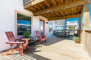 Eine Holzterrasse mit zwei Adirondack-Stühlen, einem Tisch und Kübelpflanzen.