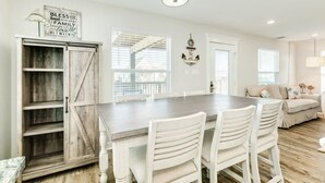 A dining area with a wooden table, white chairs, and a farmhouse-style cabinet. - Seaside Sanctuary - Adorable Beach A-Frame, Decks! (Surfside Beach)