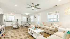 A spacious living room with a white sofa, a coffee table, and a dining area with a white table and chairs. - Seaside Sanctuary - Adorable Beach A-Frame, Decks! (Surfside Beach)