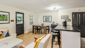 A modern living room with a dining area, kitchen, and a large island. There are framed pictures on the walls, a sofa, and a coffee table. - "Clementine at The 403" Historic District Apartment Walkable to Downtown (Natchitoches)