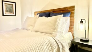 A neatly made bed with a quilted white duvet, a wooden headboard, and several pillows. There is a framed picture on the wall to the left of the bed. - "Clementine at The 403" Historic District Apartment Walkable to Downtown (Natchitoches)