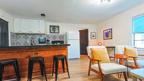A modern kitchen with white cabinets, a black and white backsplash, and a wooden bar area with stools. There is a dining area with a table and chairs, and a window with a view. - "Clementine at The 403" Historic District Apartment Walkable to Downtown (Natchitoches)