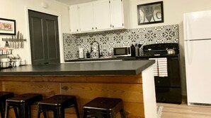 A kitchen with a wooden island, bar stools, white cabinets, a microwave, and a refrigerator. - "Clementine at The 403" Historic District Apartment Walkable to Downtown (Natchitoches)