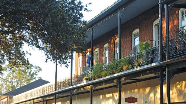 A row of storefronts with outdoor seating and plants, a brick building with a balcony, and a clear sky. - "Clementine at The 403" Historic District Apartment Walkable to Downtown (Natchitoches)