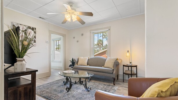 Un salon avec un ventilateur de plafond, un canapé, une table basse et un meuble pour la télévision.