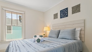 Une chambre à coucher comprenant un lit, une fenêtre, une table de chevet et des œuvres d’art décoratives au mur.