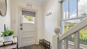 Un couloir doté d’un plancher en bois, une porte blanche avec un panneau indiquant la sortie, une petite plante posée sur un plateau et une fenêtre donnant sur un paysage verdoyant.