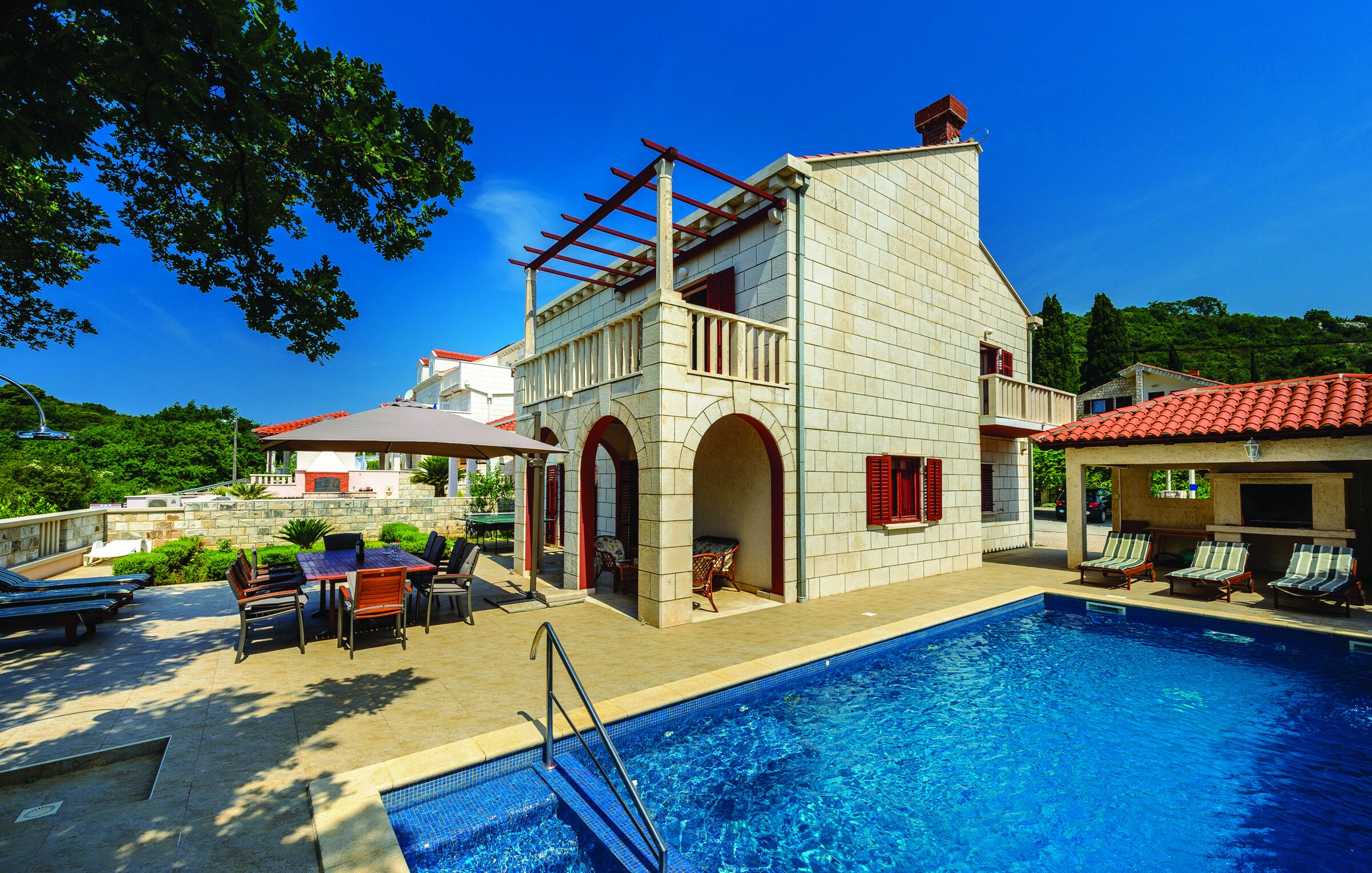A two-story building with a swimming pool, outdoor seating, and a red-tiled roof.
