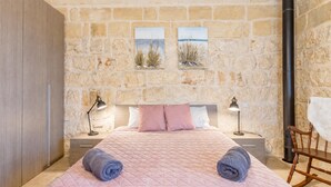 A bedroom with a stone wall, a bed with pink bedding, two bedside tables with lamps, and a chair. - Pool & SPA - Wellness Villa St Martin (Mgarr)
