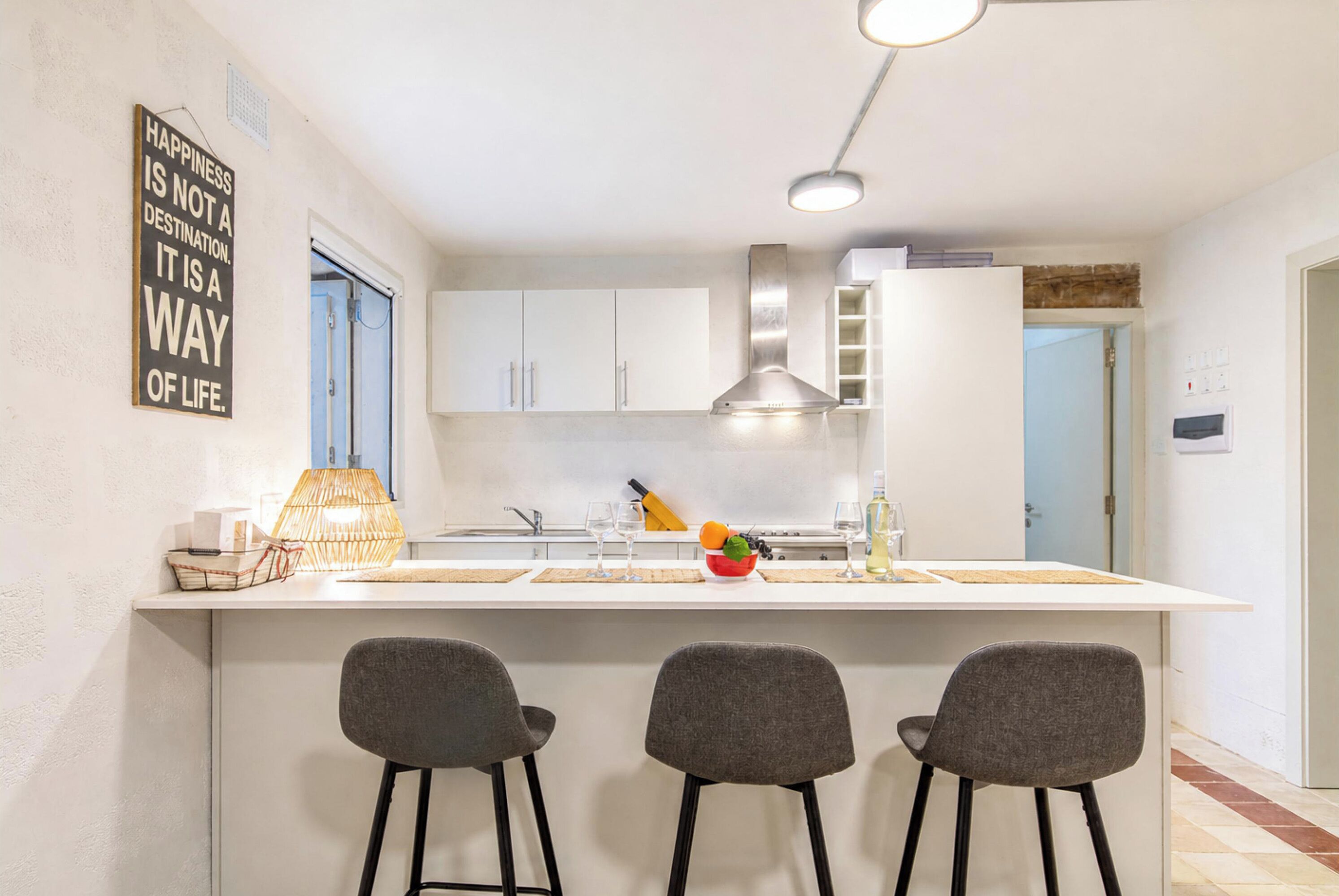 A modern kitchen with white cabinets, a central island with bar stools, and a hanging light fixture.