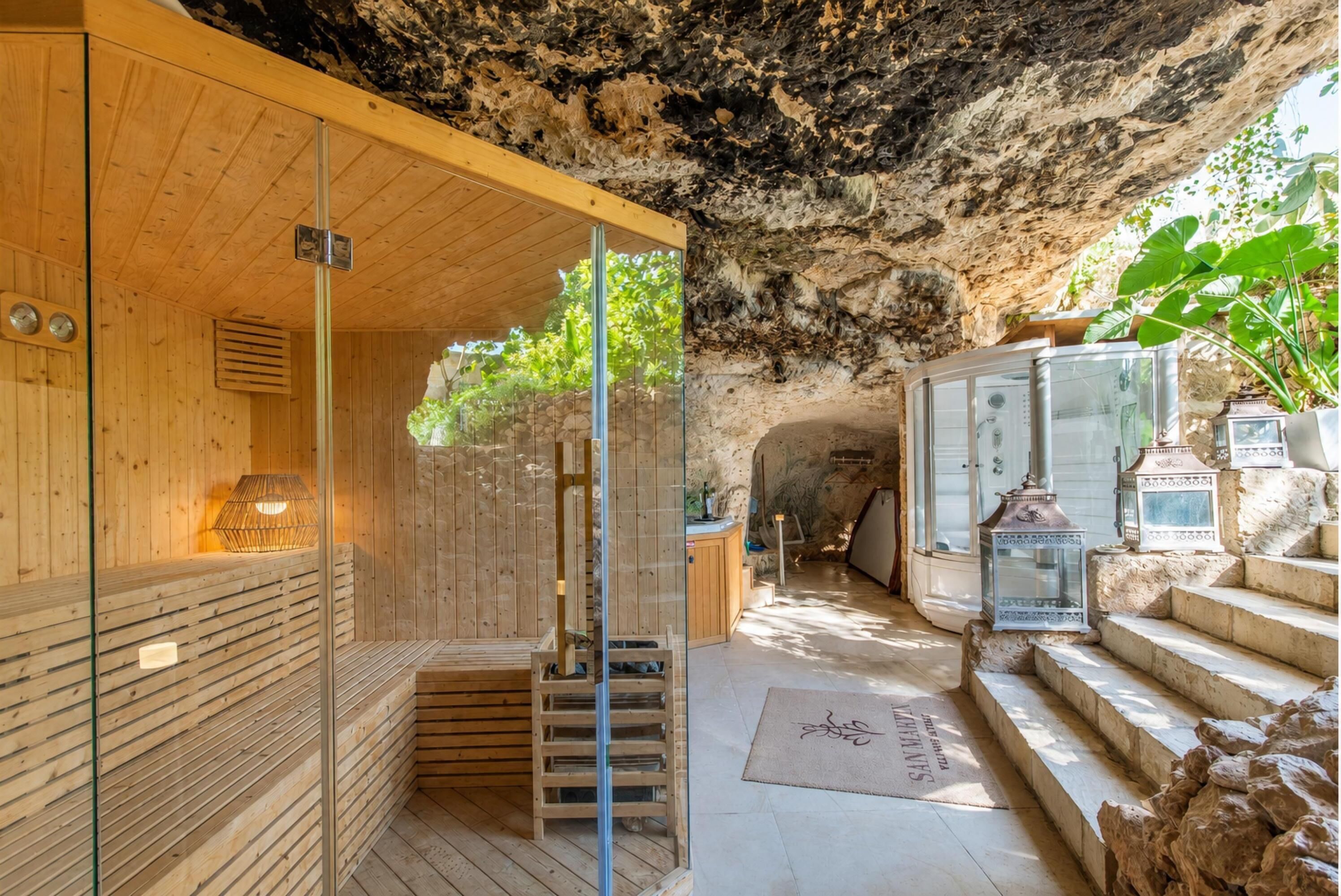 A sauna room with wooden walls and a glass door, a wooden bench, and a small table with a lamp.