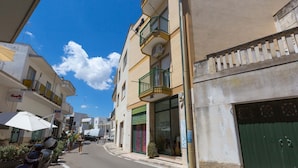 A narrow street with buildings on either side, featuring balconies with railings and a clear blue sky above. - 3038 La Casa di Maristella- Bilo by Barbarhouse (Otranto)