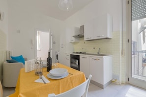 A modern kitchen with white cabinets, a yellow tablecloth, and a dining area with a white chair. - 3038 La Casa di Maristella- Bilo by Barbarhouse (Otranto)