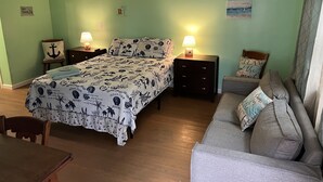 Une chambre à coucher avec un lit, deux tables de chevet, un ventilateur de plafond, un canapé gris et une table en bois.