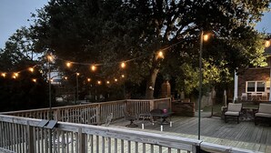 Une terrasse en bois agrémentée de guirlandes lumineuses, de meubles d’extérieur et d’une structure en briques.