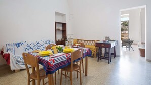 A dining area with a table set for four, a sofa, and a small kitchen area. - 2999 La Casa in Piazzetta by Barbarhouse (Castro)