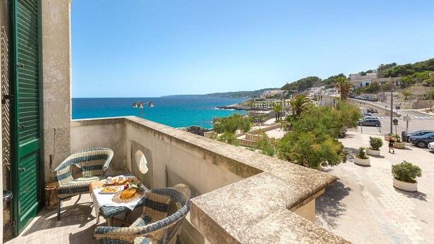 A balcony with wicker furniture, a table with food, and a view of the sea and town. - 2999 La Casa in Piazzetta by Barbarhouse (Castro)